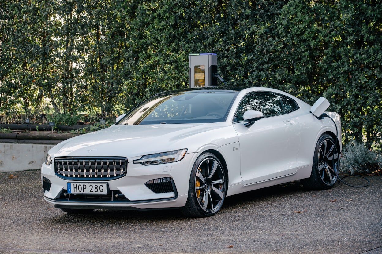 Polestar 1 in Snow White being charged at a parking lot with green trees.