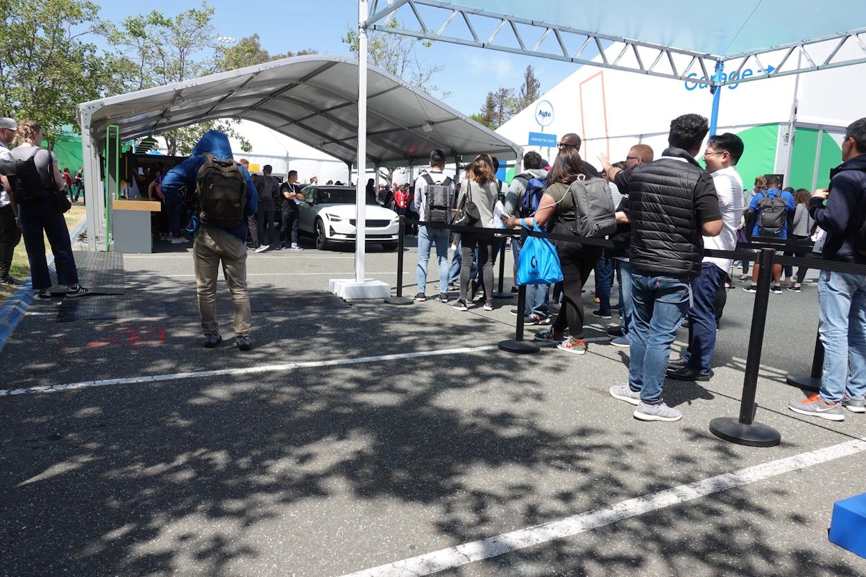 Crowd forming a queue, waiting to explore Polestar 2, which is displayed under a protective tent in a parking lot.