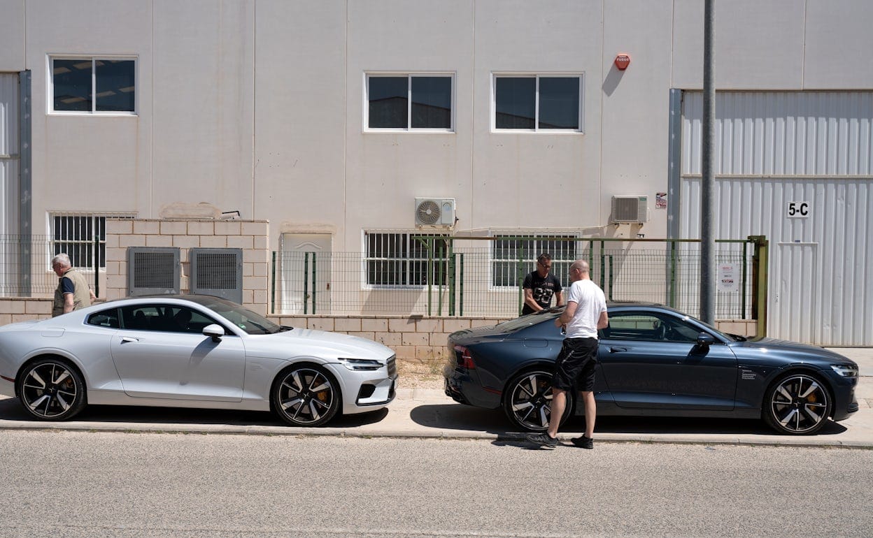 Two Polestar 1 cars parked in front of an industrial building with three men walking next to the cars.