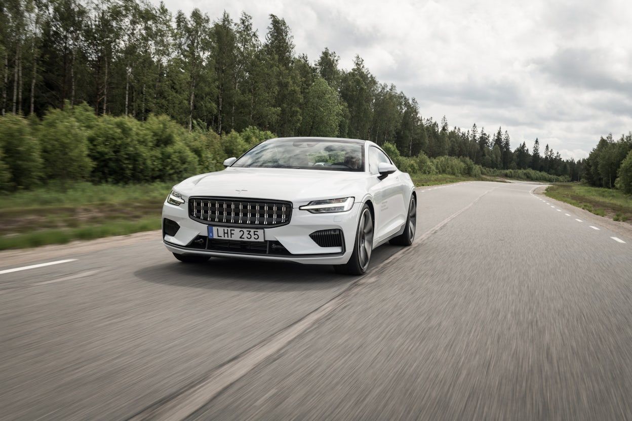 Front view of a white Polestar 1 driving on a forest road.