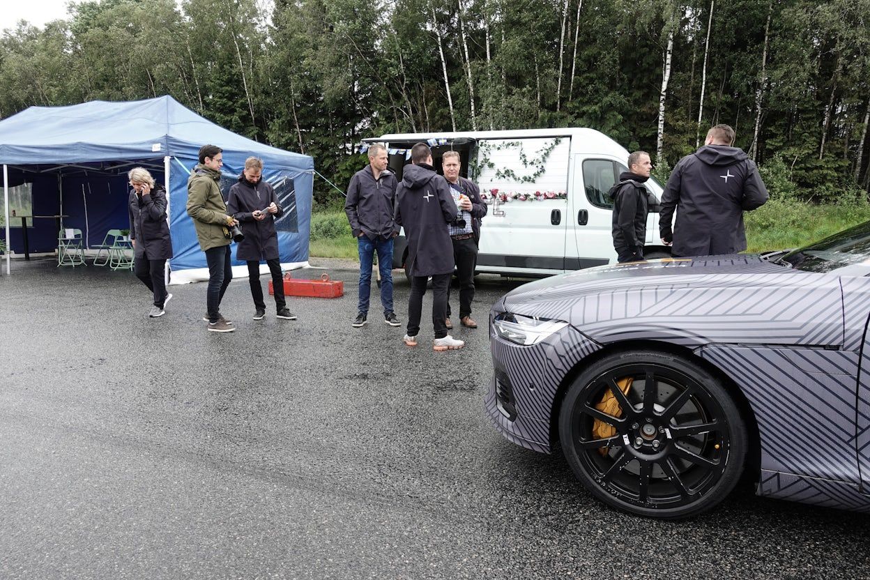 People gathered on a forest road next to a parked Polestar 1.
