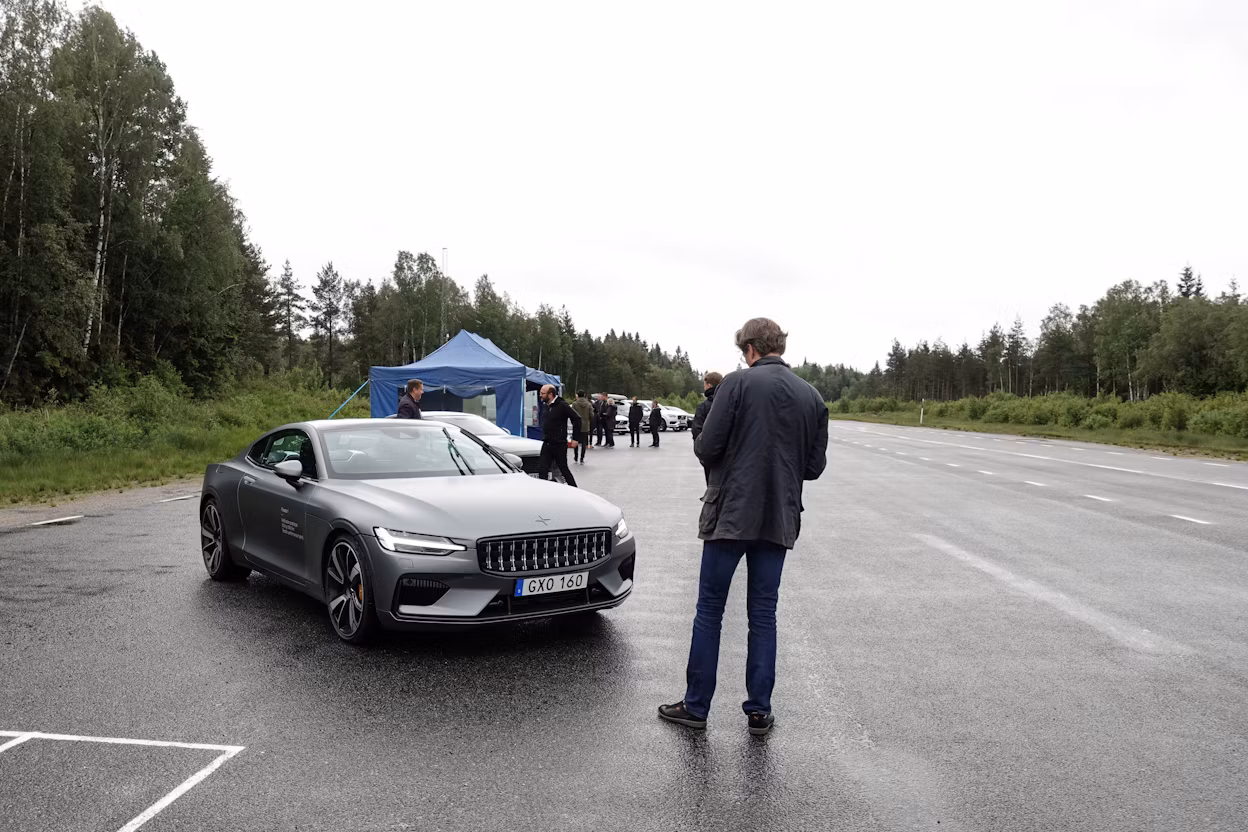 People gathered on a forest road next to a parked Polestar 1.