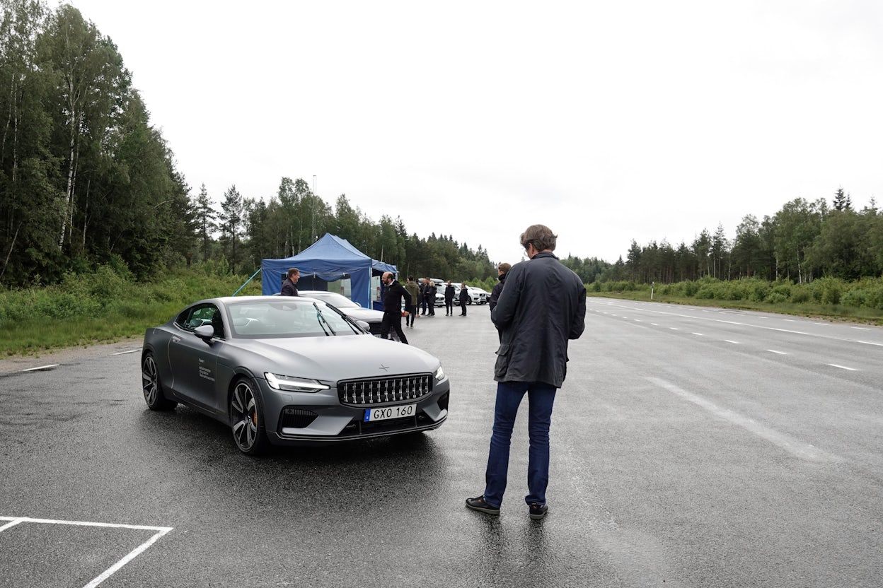 People gathered on a forest road with a parked Polestar 1
