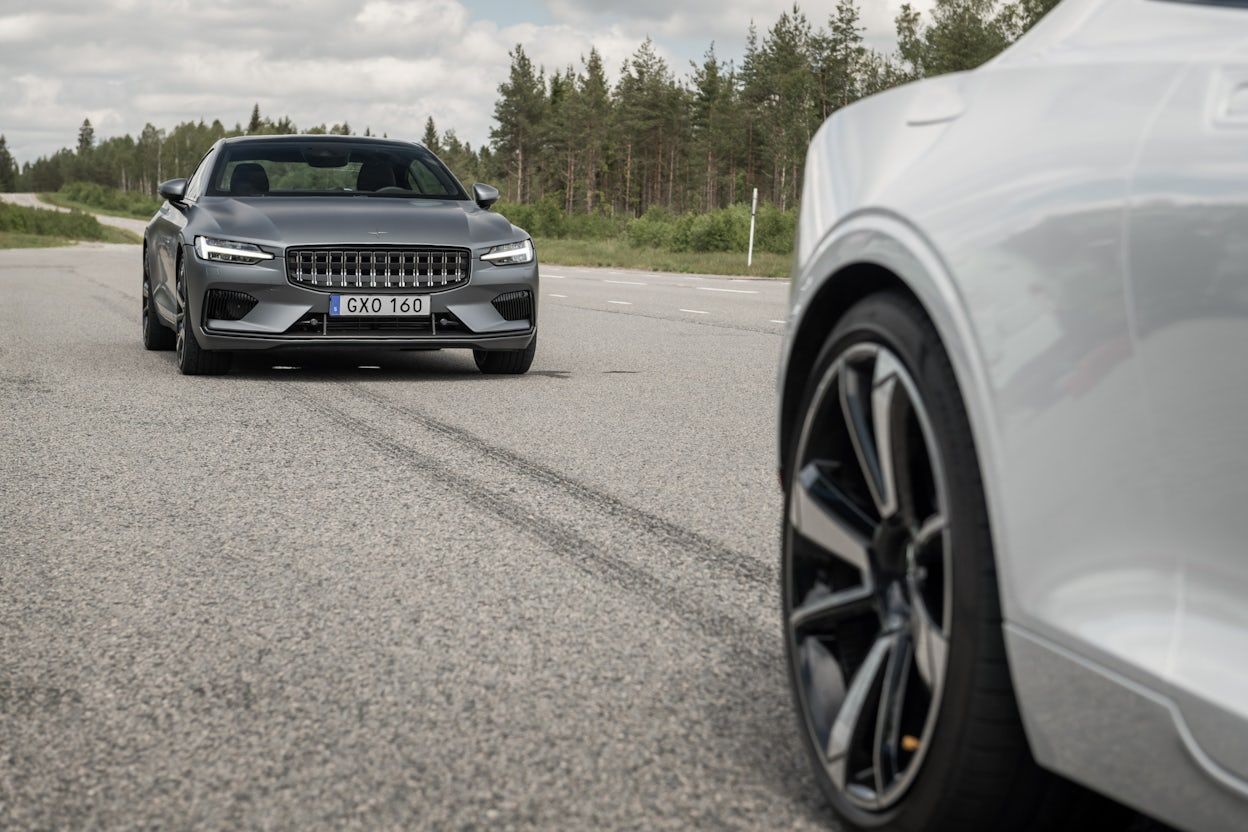 A metallic Polestar 1 and a white Polestar 1 driving on a forest road.