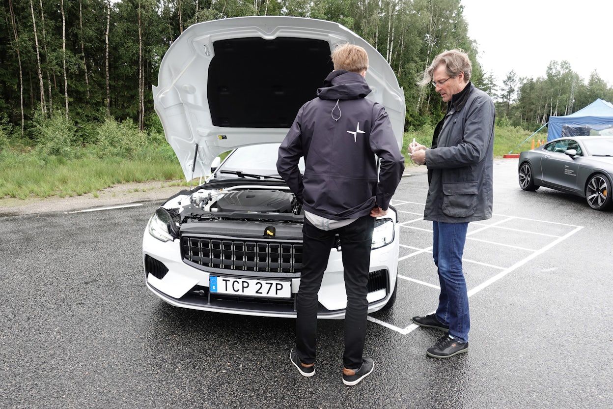 Two people in front of a white Polestar 1 with the hood open.