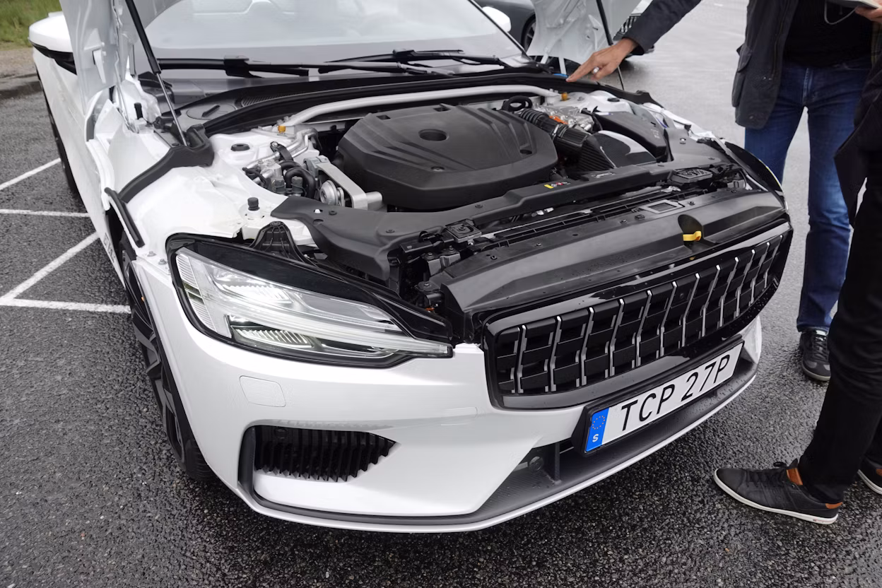A person pointing at the front of a white Polestar 1 with the hood open.