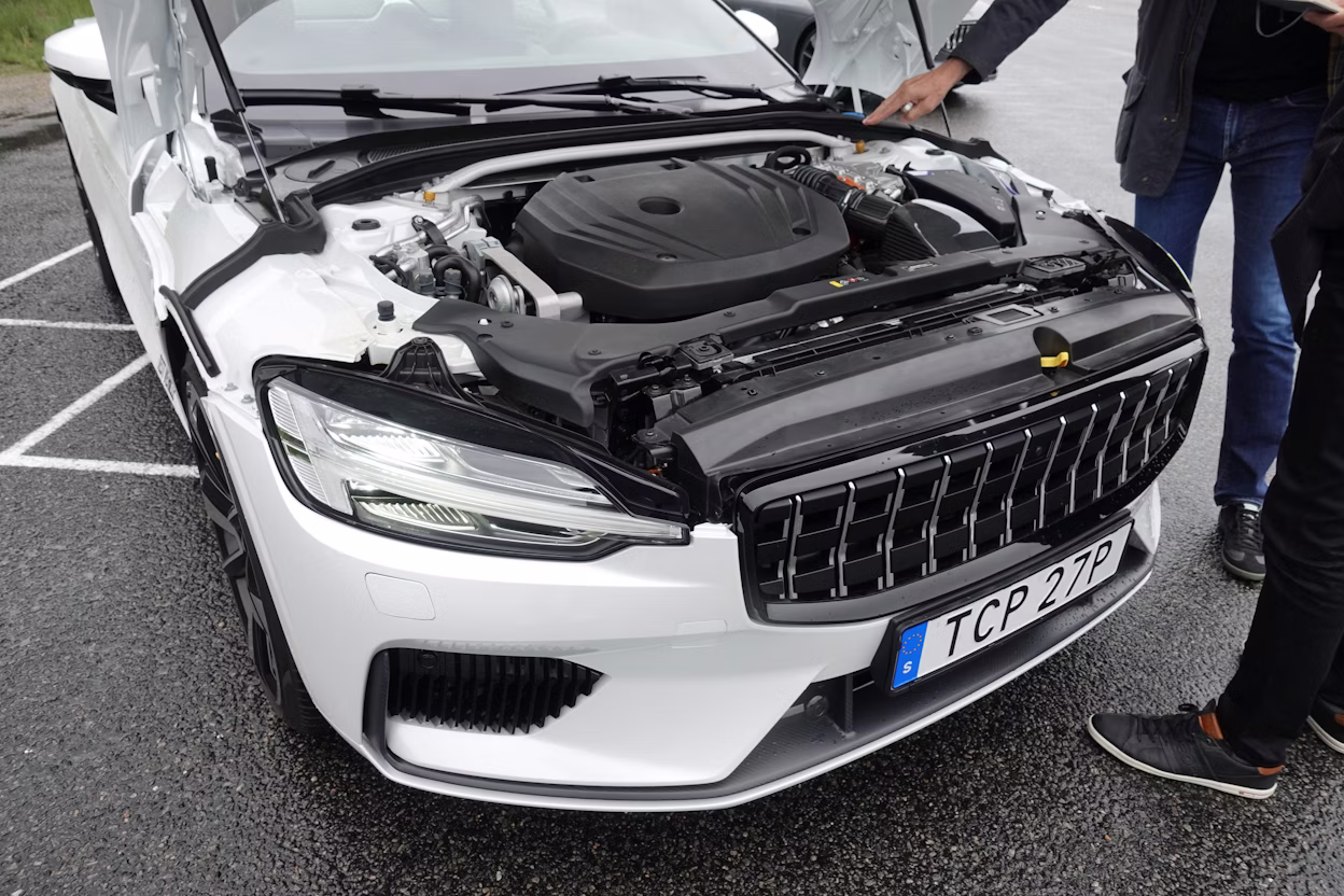 A person pointing at the front of a white Polestar 1 with the hood open.