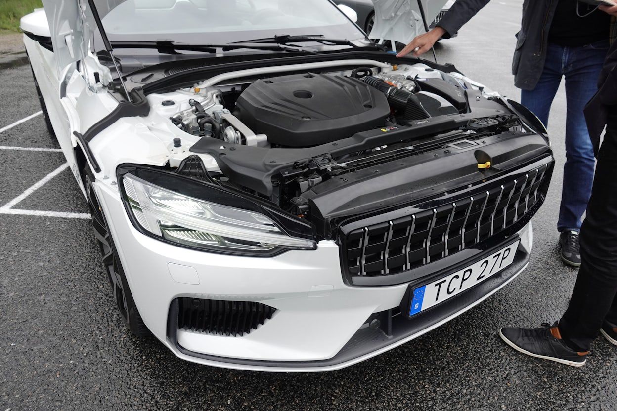 A person pointing at the front of a white Polestar 1 with the hood open