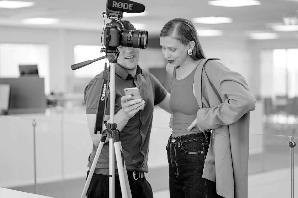 Jenny Mustard and a photographer in black and white looking at a phone in front of a camera