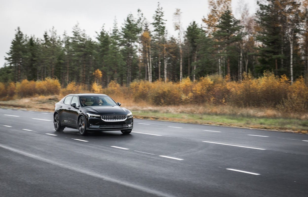 A black Polestar 2 driving on a road in autumn