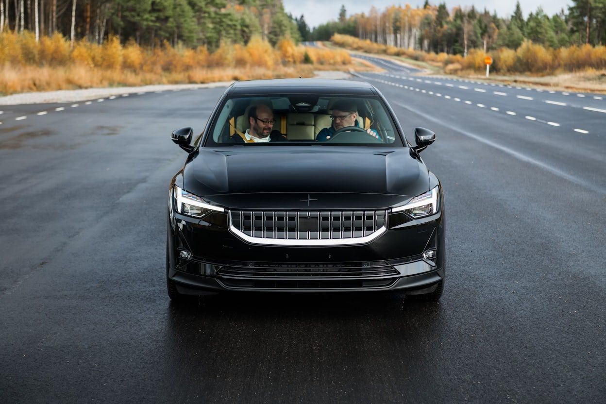 Two people sitting in the front seats of a black Polestar 2 on the road in autumn.