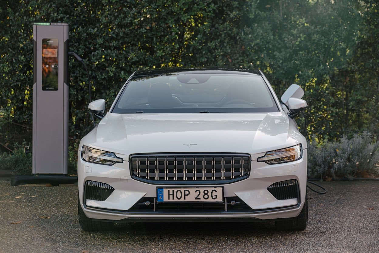 A white Polestar 1 parked next to a Siemens charging station with the charging cable connected.