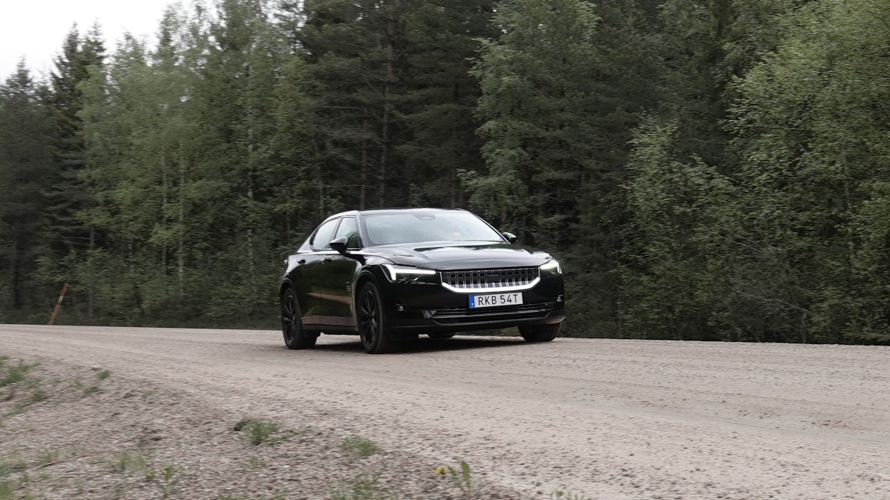 A black Polestar 2 driving on a forest road.