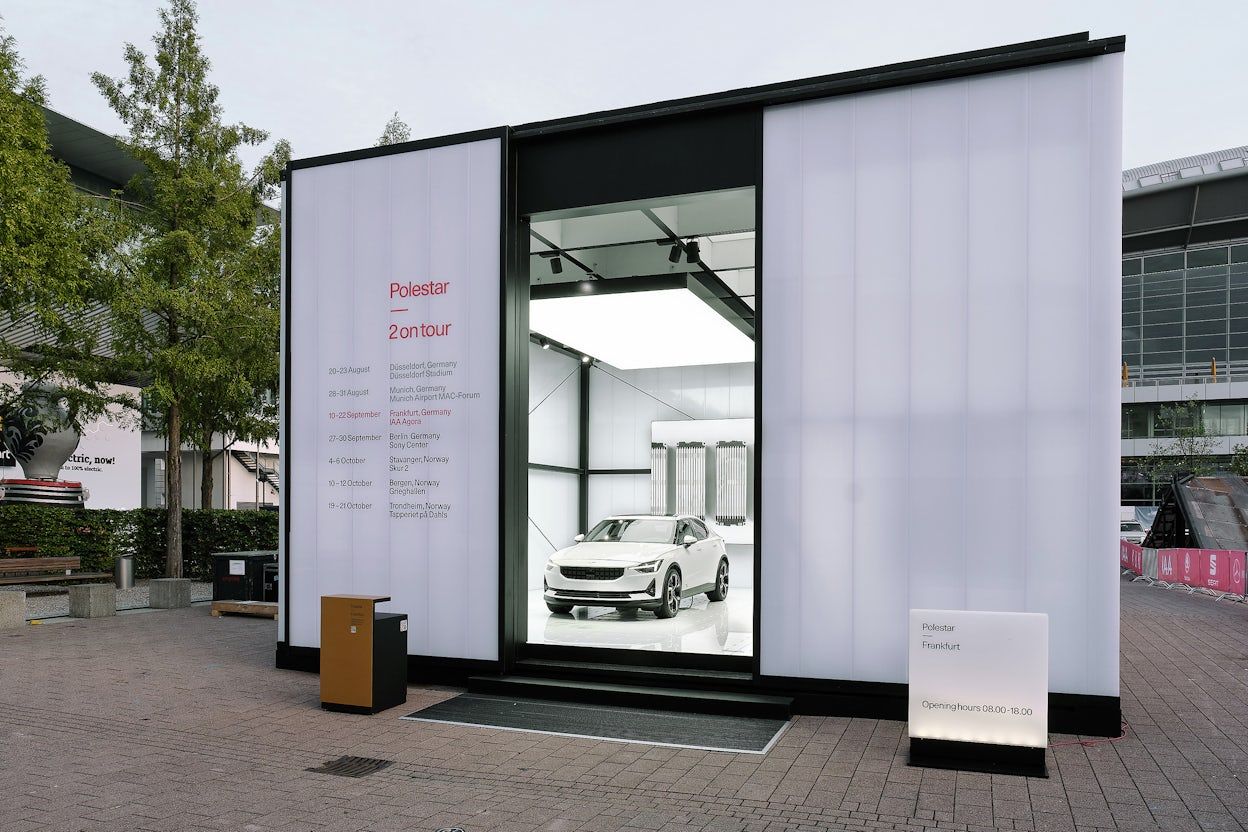 A white Polestar 2 parked in a pop-up exhibition display that has the text Polestar 2 on tour.