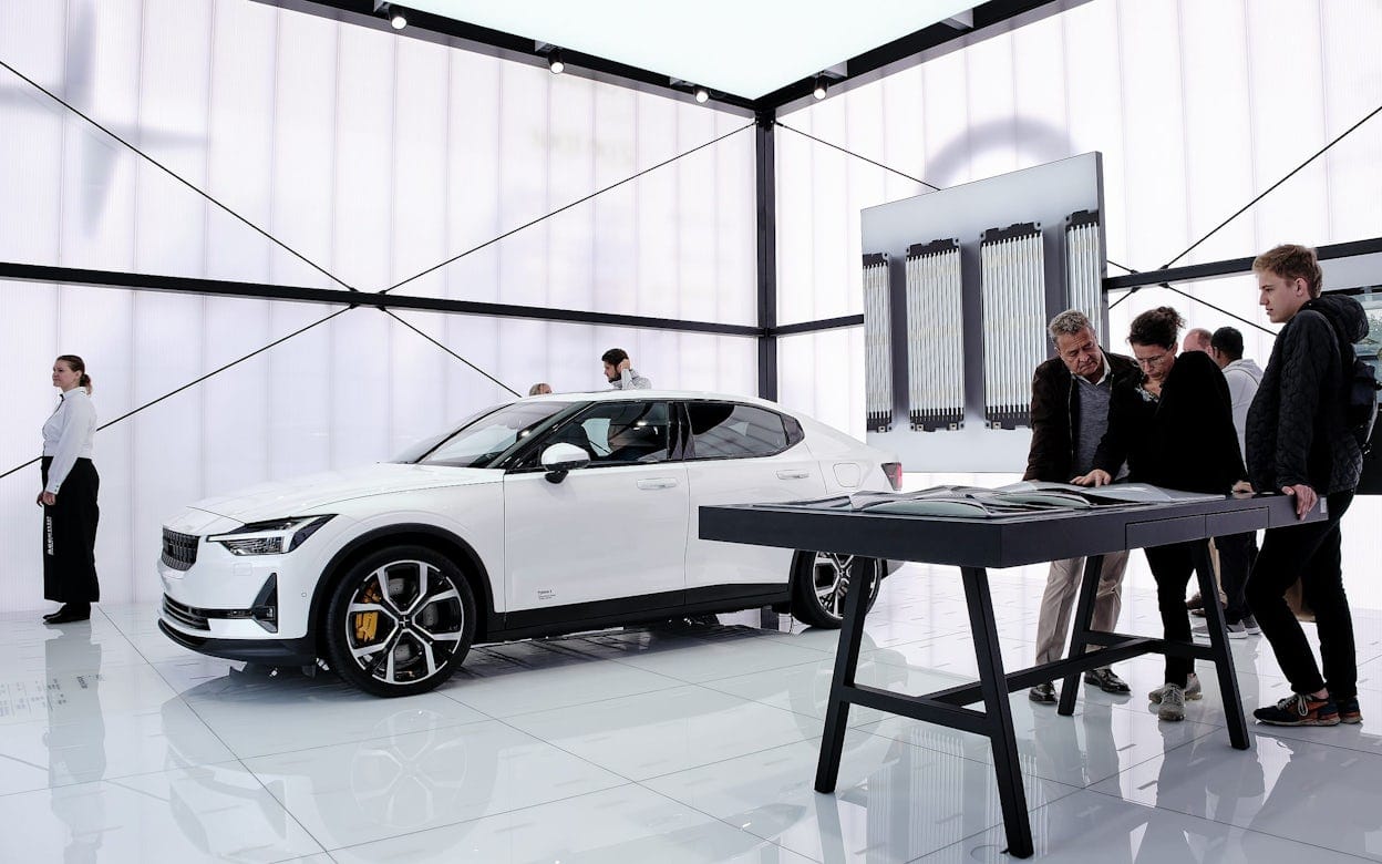 People gathered around a white Polestar 2 in a exhibition space.