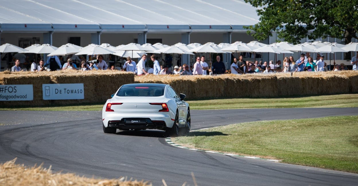 A crowd of spectators watching as a sleek white Polestar 1 speeds around the racing track at the Goodwood Festival of Speed.