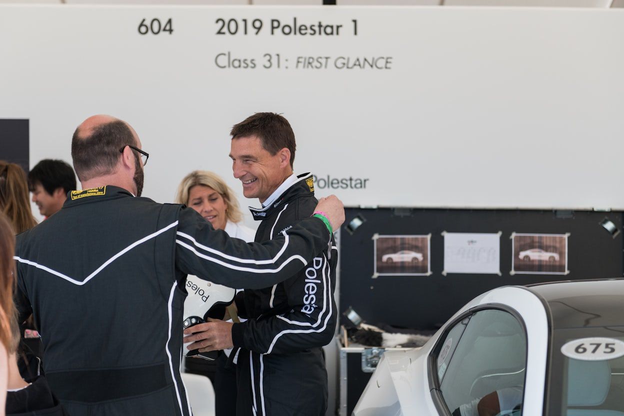 Polestar CEO Thomas Ingenlath, dressed in a racing overall, smiling whilst standing next to a Polestar 1
