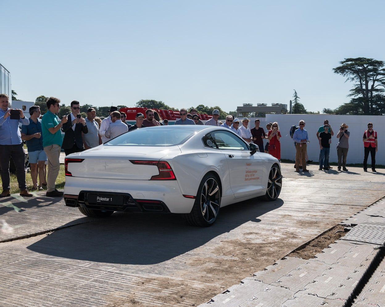 Crowd of spectators taking photos of a white Polestar 1 in a outdoor car show area.