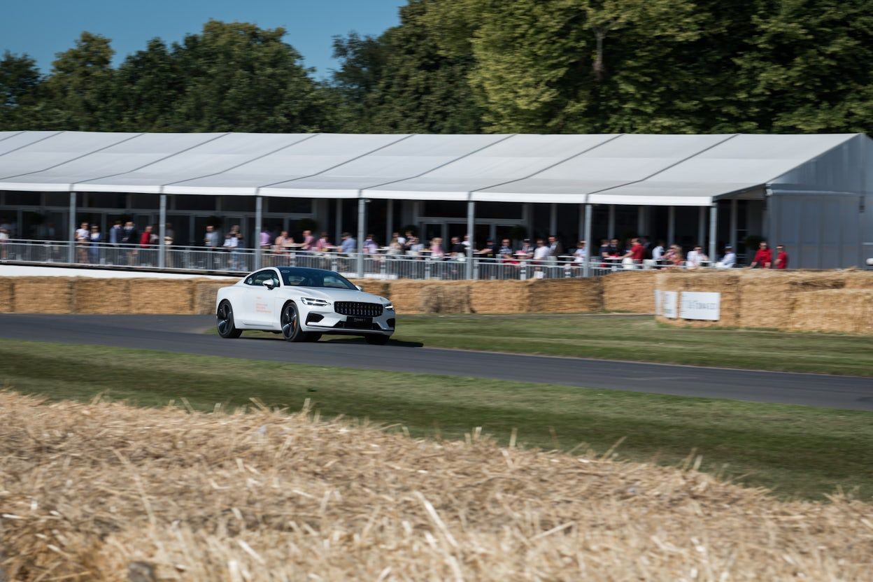 White Polestar 1 in focus as it speeds around the racing track with spectators watching in the background