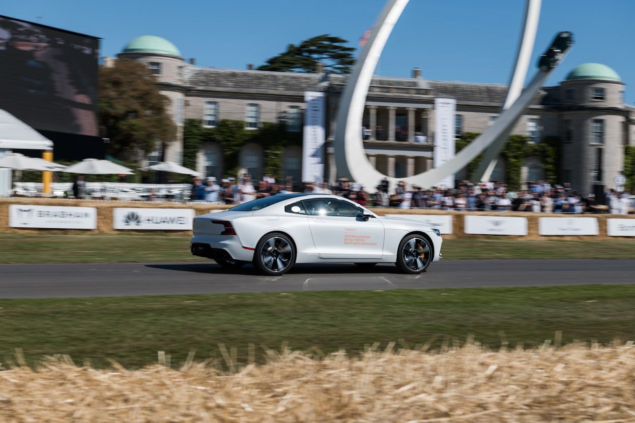 White Polestar 1 racing on the track, positioned beside a majestic castle-like building, while spectators observe from the sidelines