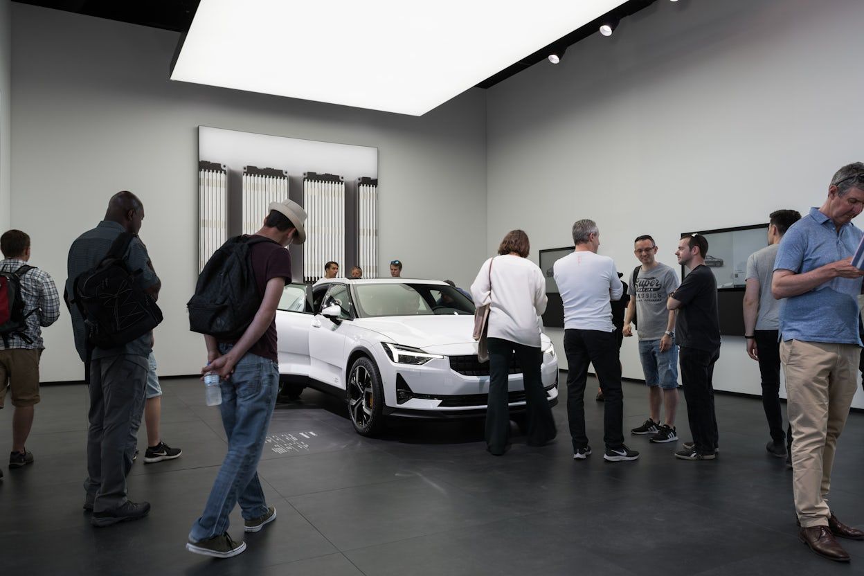 Crowd of spectators gathered around a white Polestar 2 in a minimalistic exhibition space