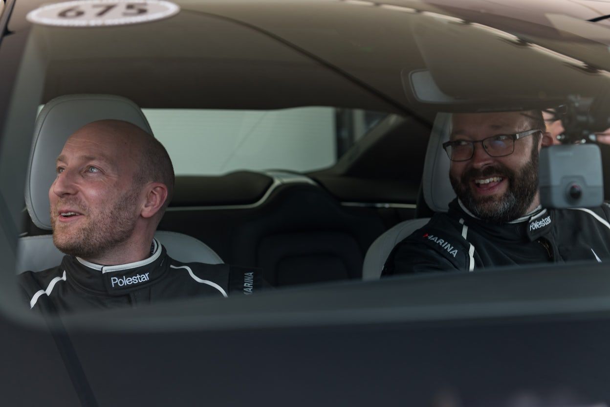 Jack Harding and Charlie May, wearing racing overalls, sit side by side in a Polestar 1 at the Goodwood Festival