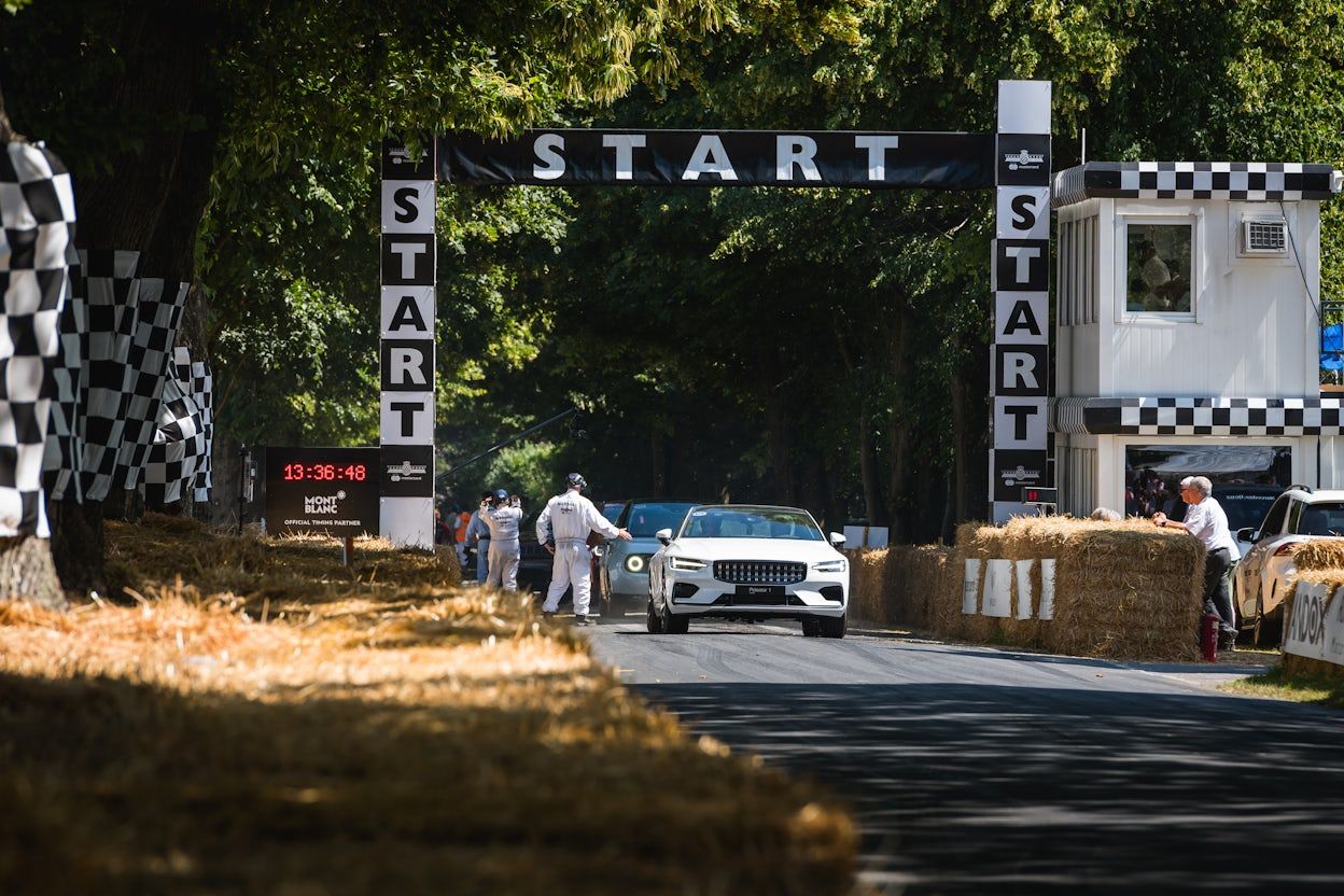 Race marshal signals as a white Polestar 1 accelerates past the starting line on the race track of the Goodwood Festival