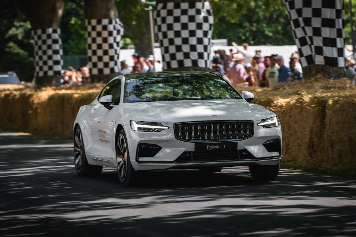 Pristine white Polestar 1 on race track with event crowd watching in the background.