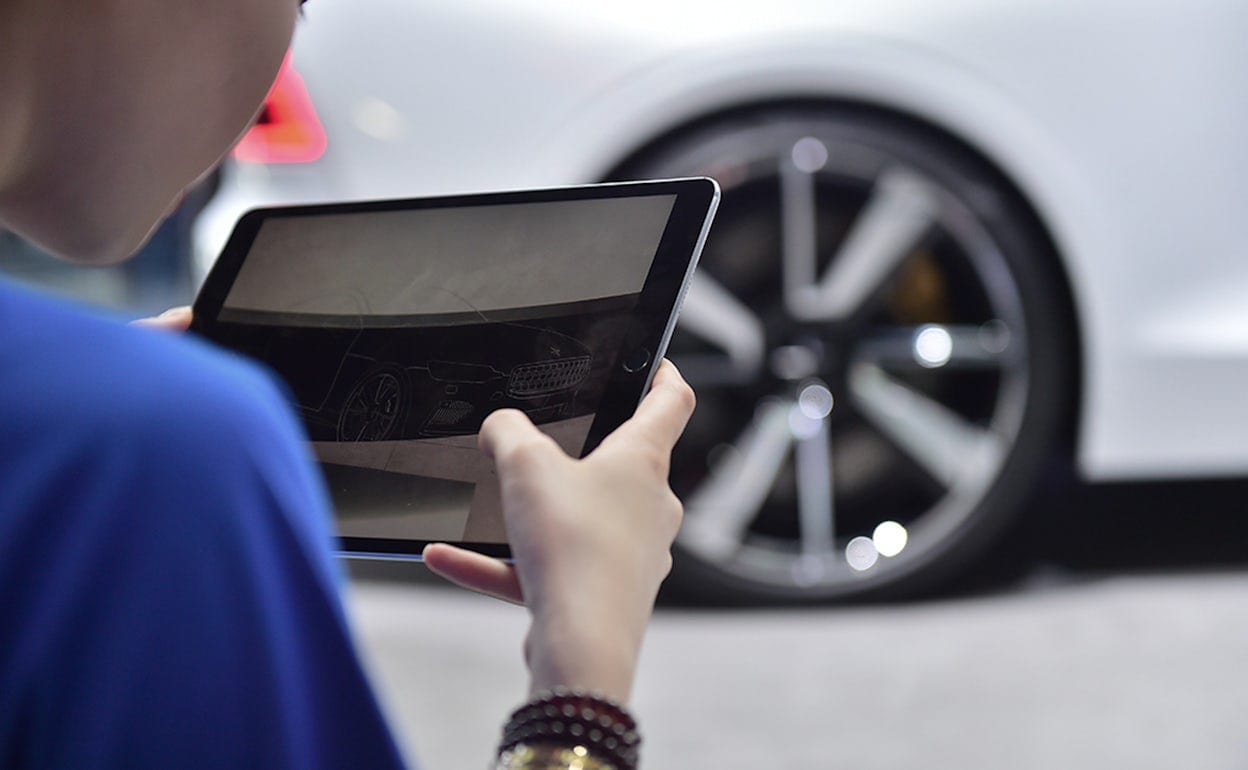 Hands holding a tablet, with a blurry Polestar 1 in the background.