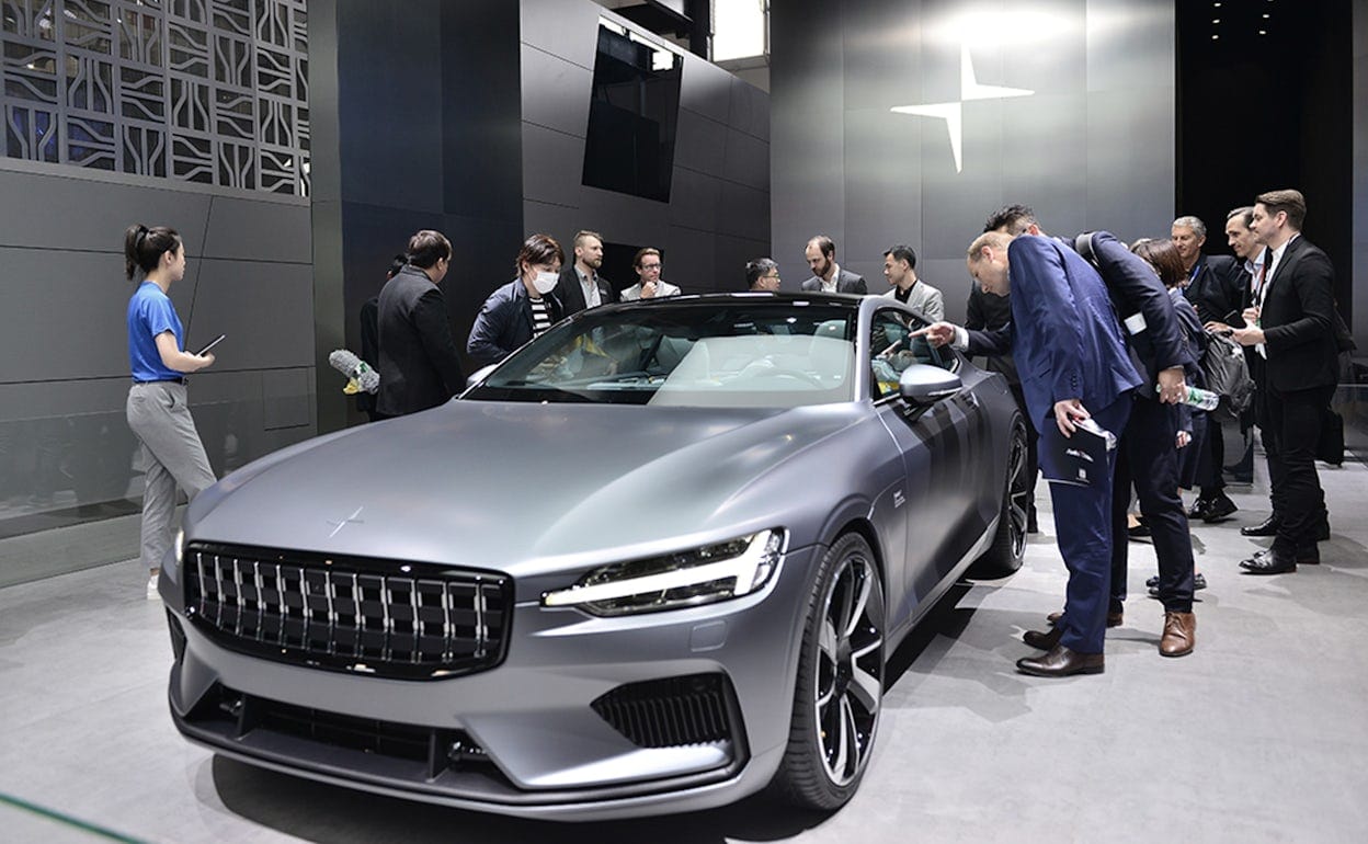 Men in suits inspecting a metallic Polestar 1 at a car event.