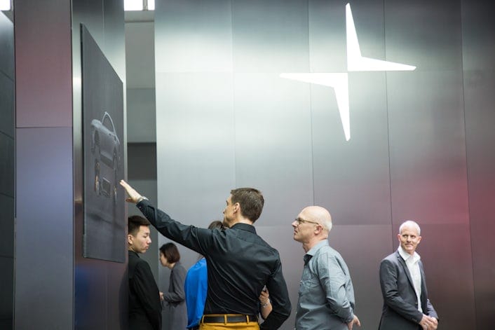 Two people looking at a picture of a Polestar on a black wall with the Polestar logo on another wall
