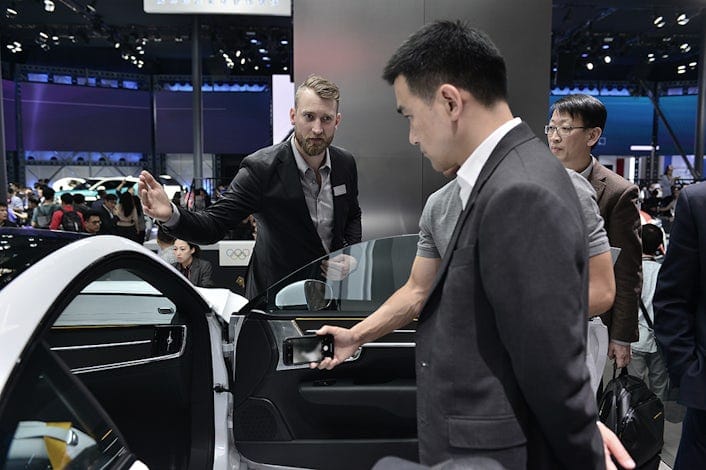 Three men inspecting a white Polestar at a car event.