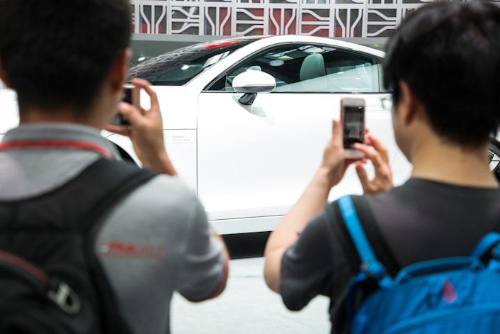 Two men photographing a white Polestar 1 at a car event.