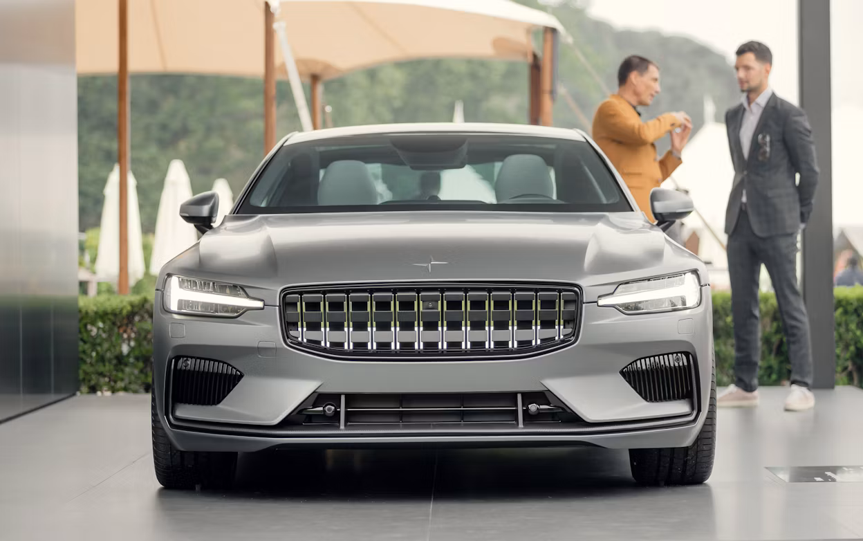 Front view of a silver Polestar 1 with two men talking in the background.