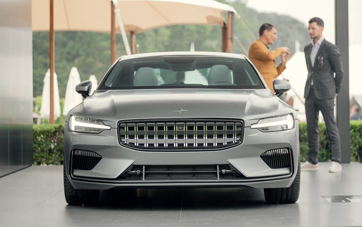 A parked Polestar 1 in silver with two people talking in the background