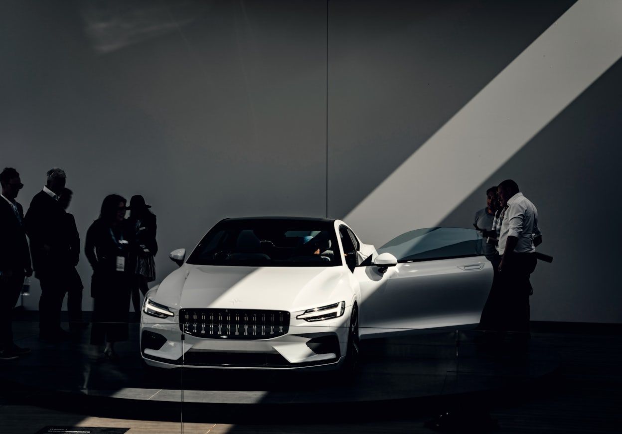 People inspecting a white Polestar 1 on display with its left door open.