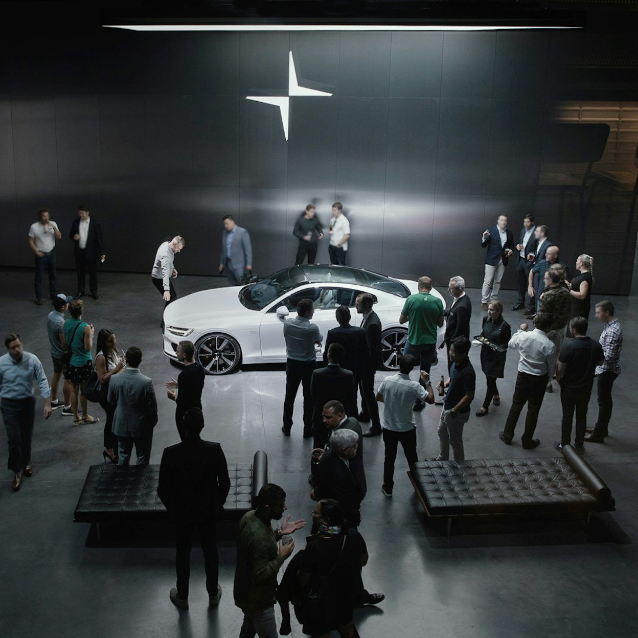 A crowd gathered around a white Polestar with the Polestar logo on a black wall in the background.