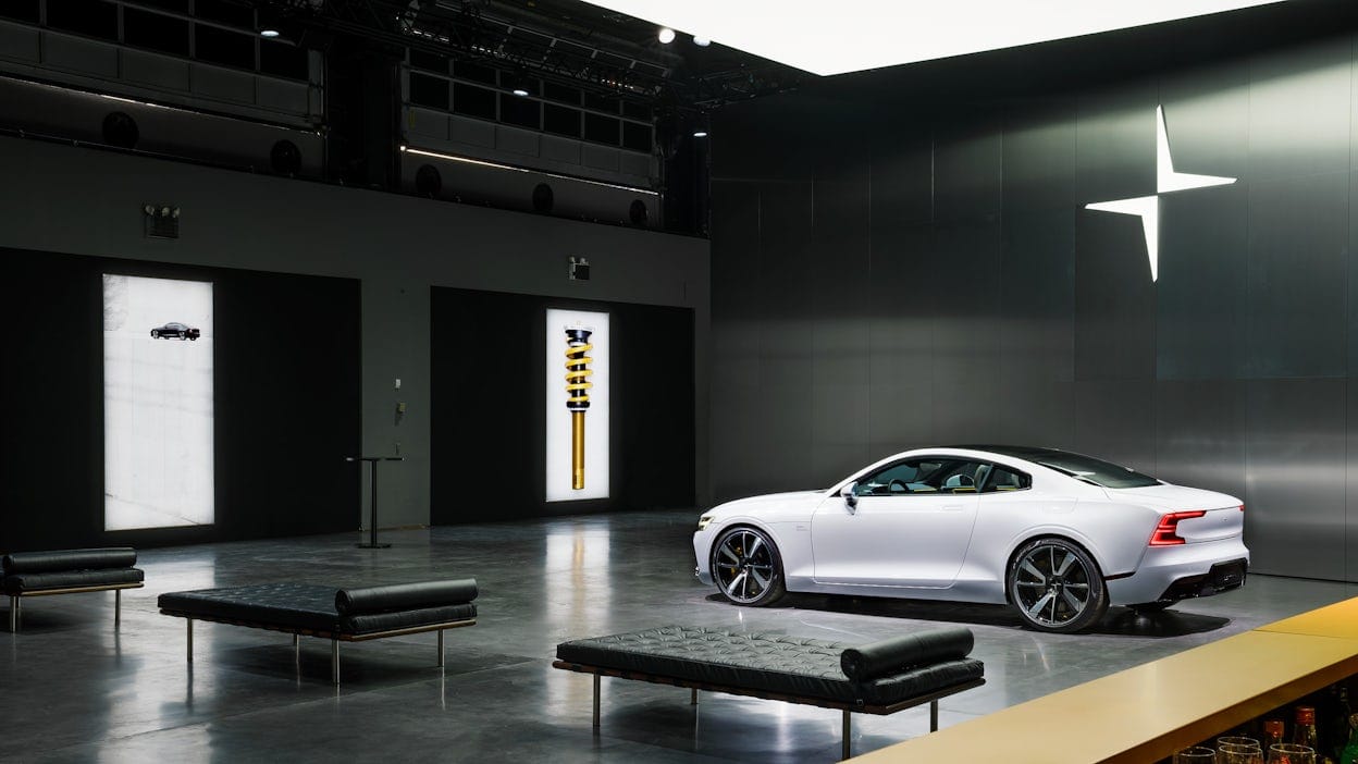 A white Polestar parked in a black room with the Polestar logo on the wall