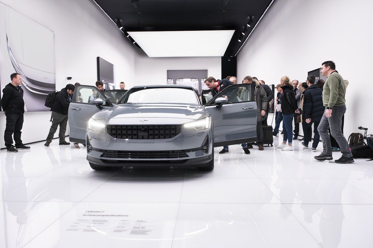Front view of a silver Polestar with the front doors open, surrounded by people.