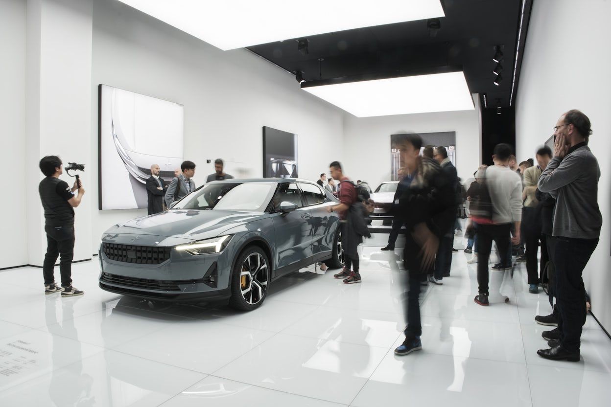 A silver Polestar surrounded by people in a white, minimalistic Polestar space.