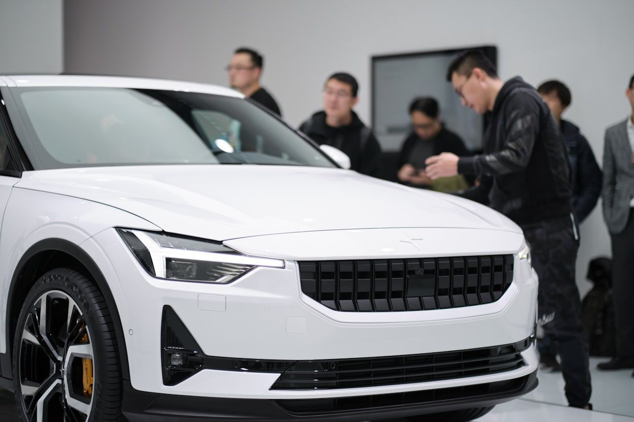 A white Polestar in focus with people in the background