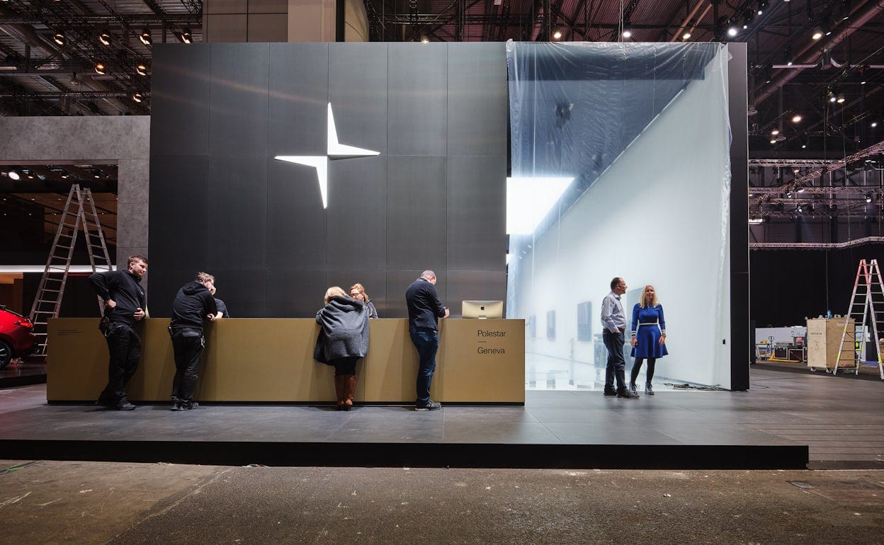 A golden reception desk with the text Polestar Geneva, and a exhibition space behind.