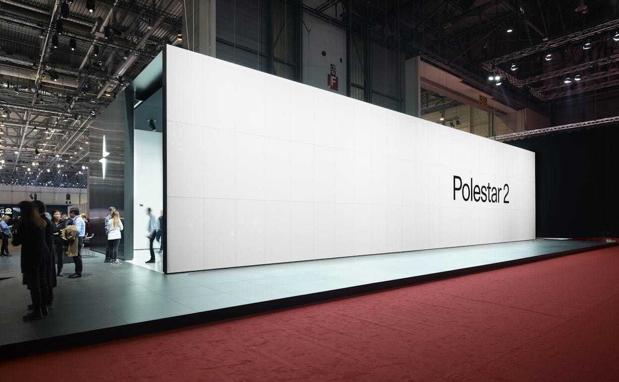 A black and white Polestar 2 stand in a big room with red carpet