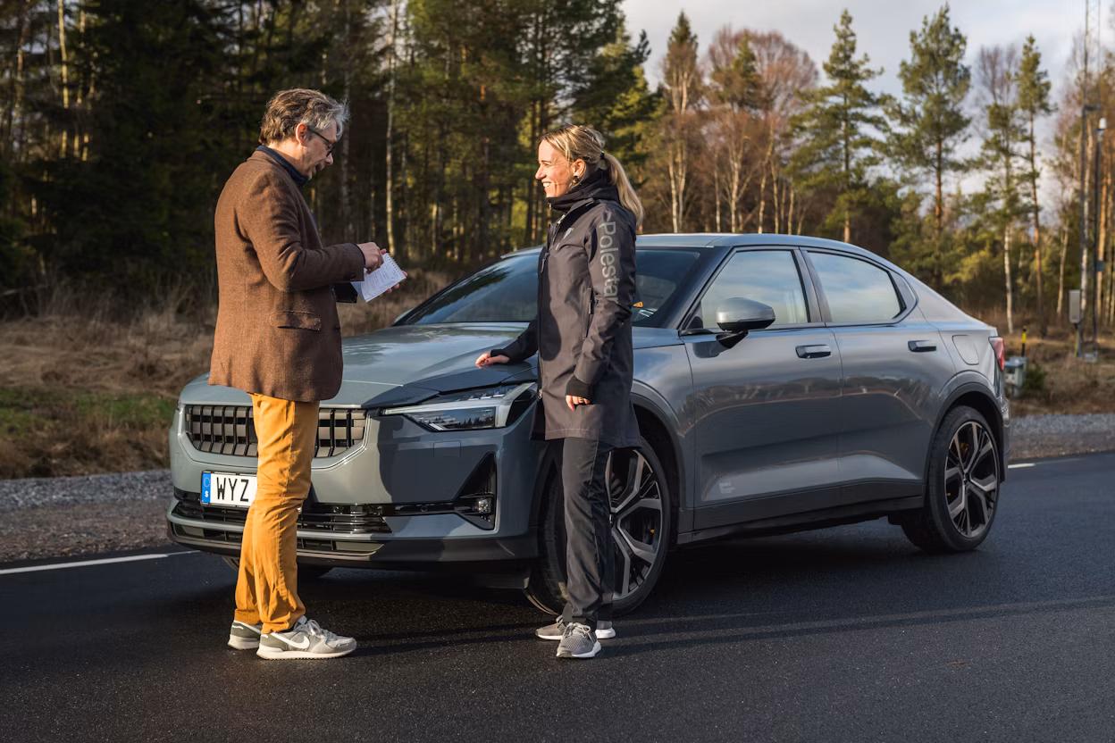 Man and woman standing in front of a parked Polestar 2 on a forest road.