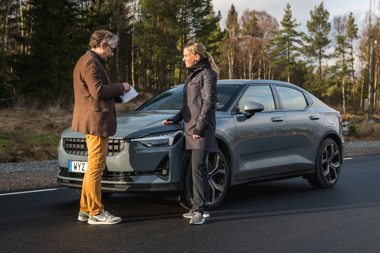 Man and woman standing in front of a parked Polestar 2 on a forest road.
