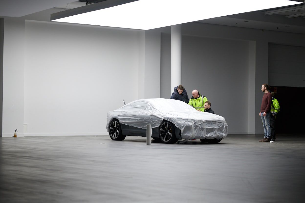 A Polestar covered in protective plastic being inspected by four men.