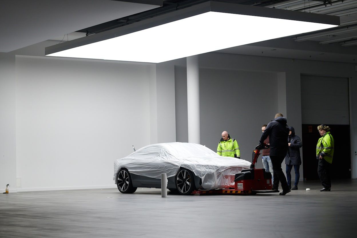 A Polestar 1 covered in white protective plastic being inspected by five men.