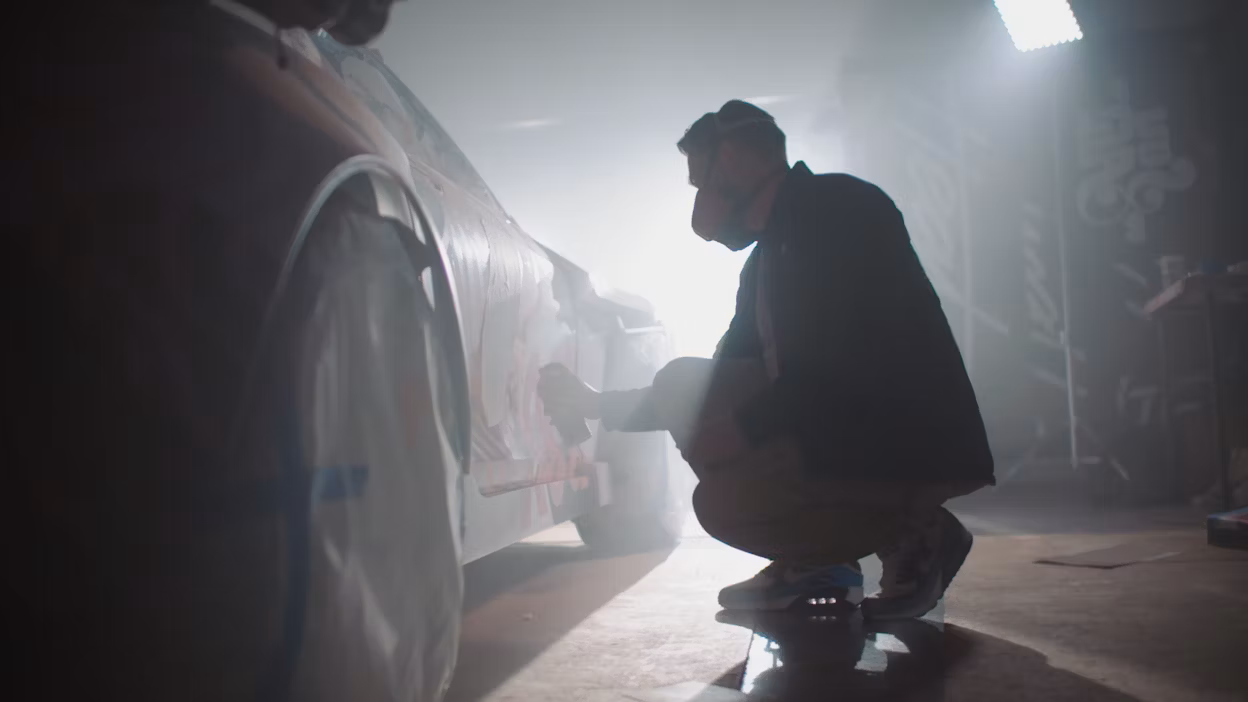 Tristan Eaton wearing a facemask while doing graffiti on a Polestar 1.