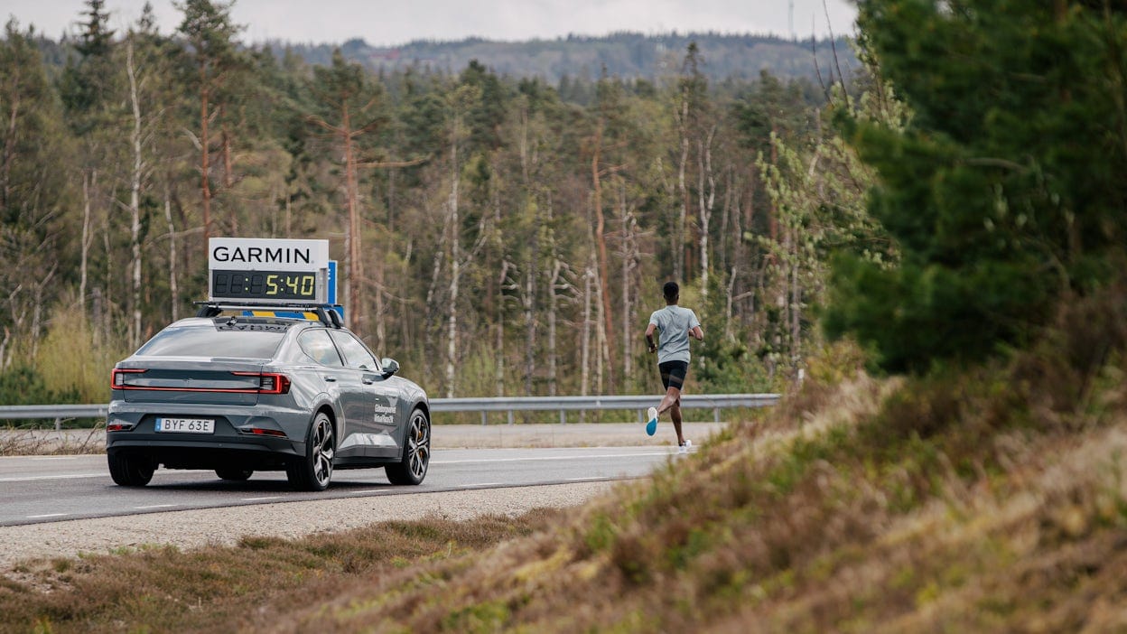 Suldan Hassan running in front of a Polestar 2 on a forest road.