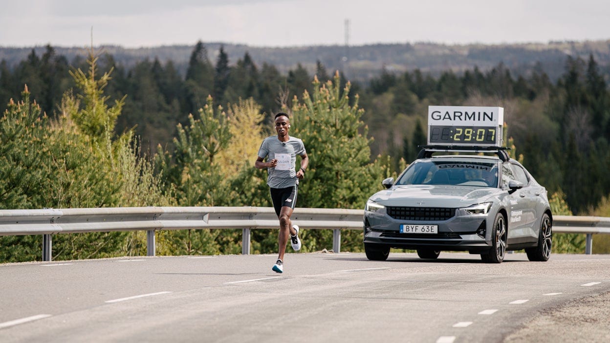 Suldan Hassan running in front of a Polestar 2 with a Garmin time counter mounted on the roof.